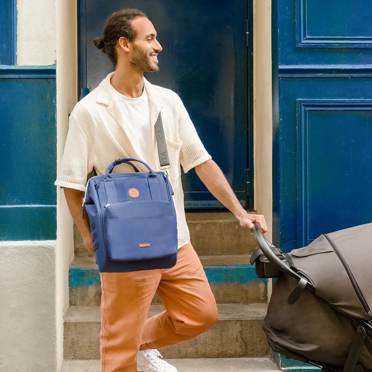 Papa portant le sac à langer Cabaïa en bandoulière en poussant la poussette en ville