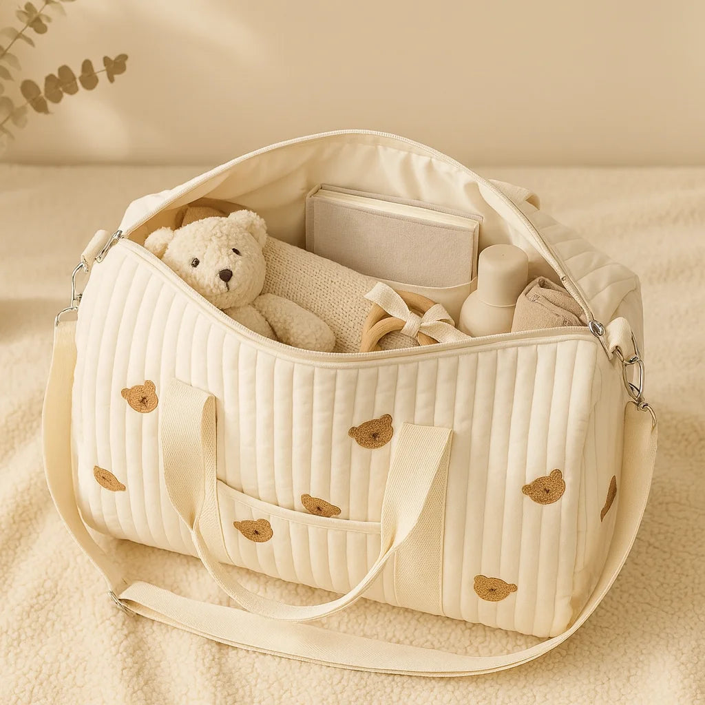 Sac à langer brodé animaux ouvert rempli d'affaires bébé (peluche, biberon, plaid)